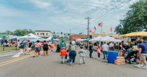 A bustling street fair with crowds, tents, and flags, showcasing vendors and families enjoying the event.