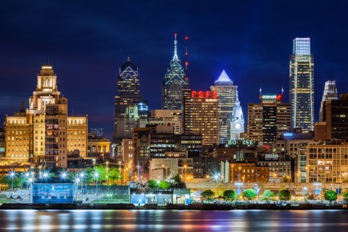 Philadelphia skyline at night, featuring illuminated buildings and reflections on the water.