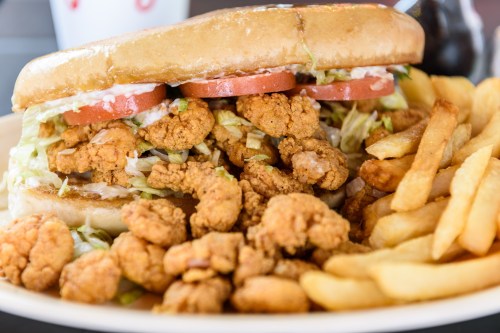 A sandwich filled with fried chicken, lettuce, and tomatoes, served with a side of golden fries.