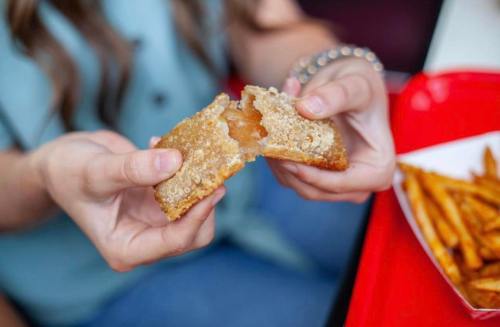A person holds a crispy, golden-brown pastry filled with a gooey filling, alongside a tray of fries.