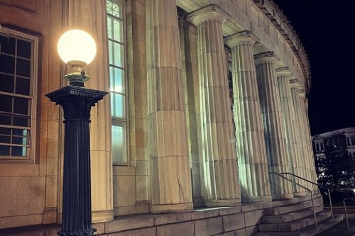 Night view of a building with tall columns, illuminated by a streetlamp in the foreground.