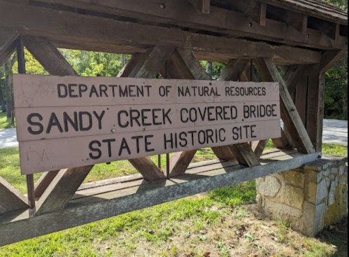 Sign for Sandy Creek Covered Bridge State Historic Site, featuring wooden structure and natural surroundings.