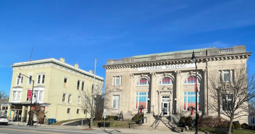 Historic Federal Building with decorative windows, flanked by a smaller yellow building under a clear blue sky.