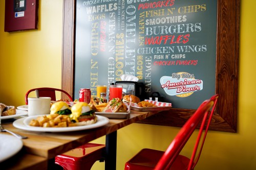 A vibrant diner scene featuring a table with breakfast dishes and a colorful menu board in the background.