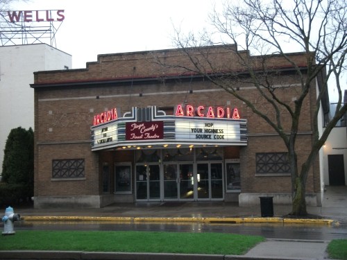 Historic Arcadia theater with a marquee displaying movie titles, surrounded by trees and a wet street.