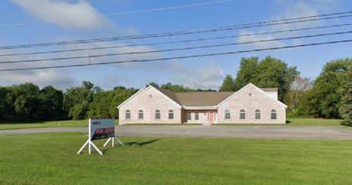A single-story brick building for lease, surrounded by green grass and trees, with a "For Lease" sign in front.