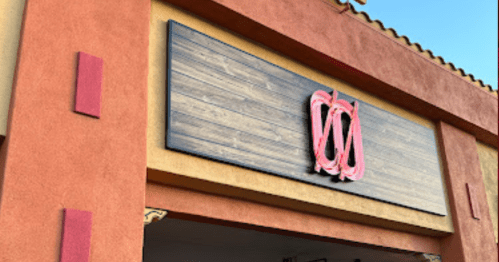 A building exterior featuring a wooden sign with a stylized logo in pink against a colorful wall.