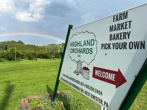 Sign for Highland Orchards with a rainbow in the background, promoting farm market, bakery, and pick-your-own options.