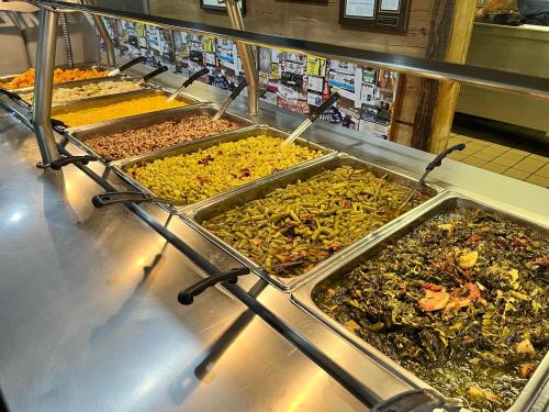 A buffet line featuring various trays of colorful side dishes, including beans, greens, and corn.
