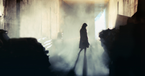 A silhouette of a person standing in a foggy corridor, with light streaming in from the end.