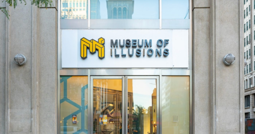 Exterior of the Museum of Illusions, featuring a modern sign and glass entrance in an urban setting.