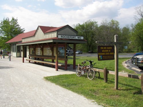 A small train station in Rocheport, MO, with a bike parked outside and green trees in the background.