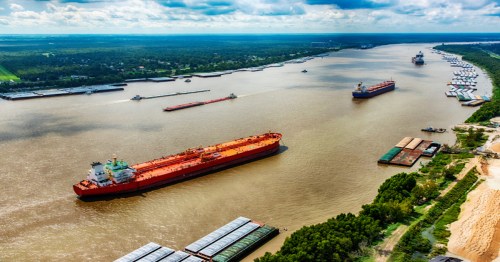 Aerial view of a river with multiple cargo ships and barges navigating through lush green banks.