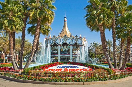 A colorful fountain with palm trees and flowers in front of a carousel at California's Great America amusement park.