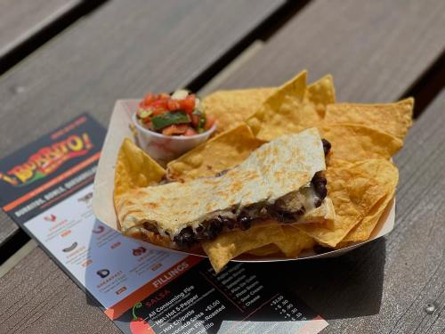 A plate of tortilla chips with a quesadilla and a small bowl of salsa on a wooden table.