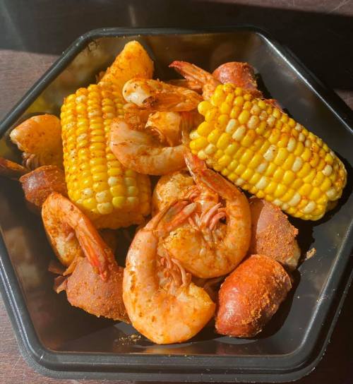 A black container filled with seasoned shrimp, corn on the cob, and small pieces of sausage.