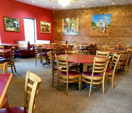 Cozy restaurant interior with wooden tables, chairs, and colorful wall art on exposed brick.