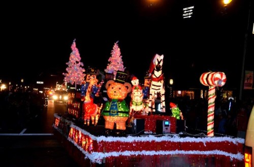 A festive parade float featuring colorful decorations, including animals, trees, and candy canes, illuminated at night.