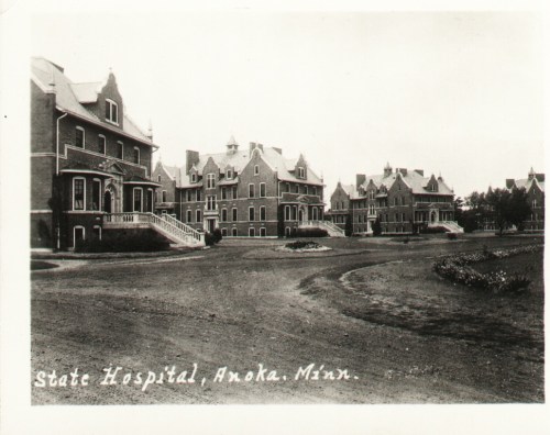 Historic black-and-white photo of the State Hospital in Anoka, Minnesota, featuring large brick buildings and landscaped grounds.