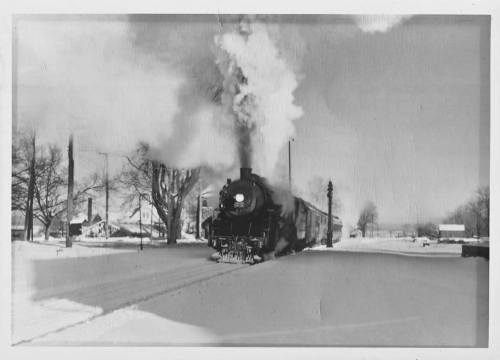 A vintage steam locomotive billows smoke while traveling through a snowy landscape.