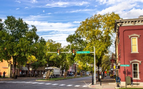 A quaint street scene with trees, a traffic light, and a red building at the corner of Central Ave on a sunny day.