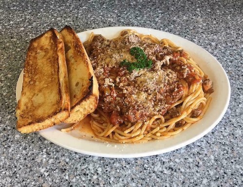 A plate of spaghetti topped with meat sauce and grated cheese, served with two slices of garlic bread on the side.
