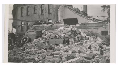 A large pile of rubble and debris from a collapsed building, with remnants of bricks and a vehicle visible.