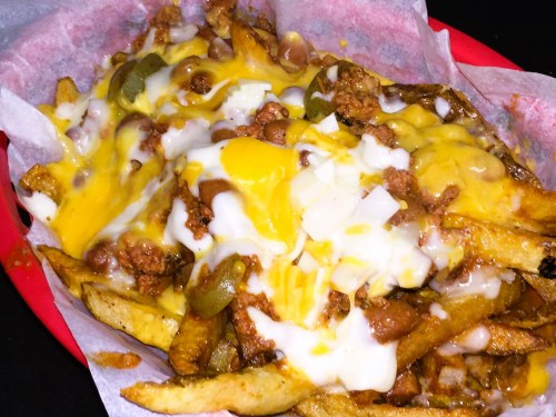 A plate of loaded fries topped with cheese, ground meat, jalapeños, and a drizzle of sauce.