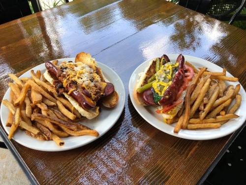 Two plates of hot dogs with toppings and a side of golden fries, set on a wooden table.