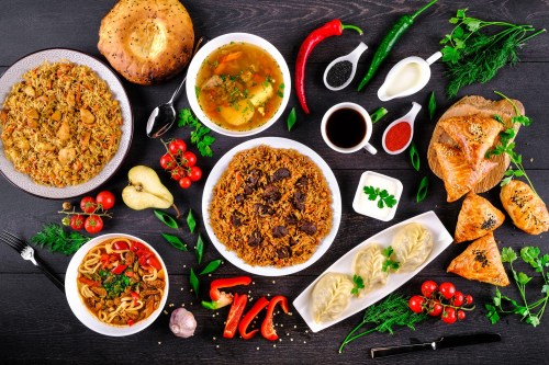 A vibrant spread of various dishes, including rice, soup, dumplings, and bread, garnished with fresh herbs and vegetables.