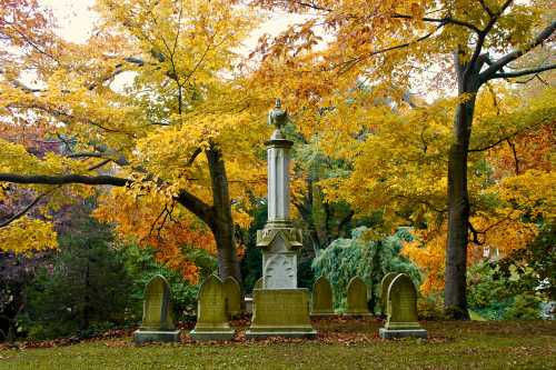 A tall monument surrounded by gravestones, set against vibrant autumn foliage in a serene cemetery.