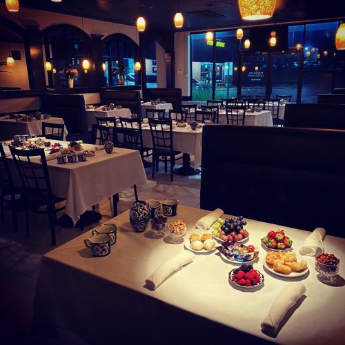 A cozy restaurant interior with neatly set tables, featuring a variety of desserts and fruits on display.