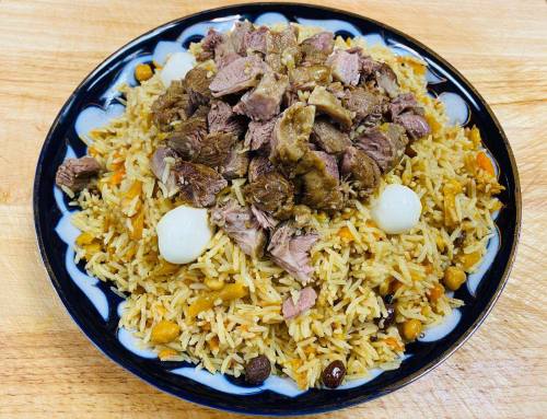 A plate of rice topped with chunks of meat, garnished with small white eggs and mixed with nuts and spices.