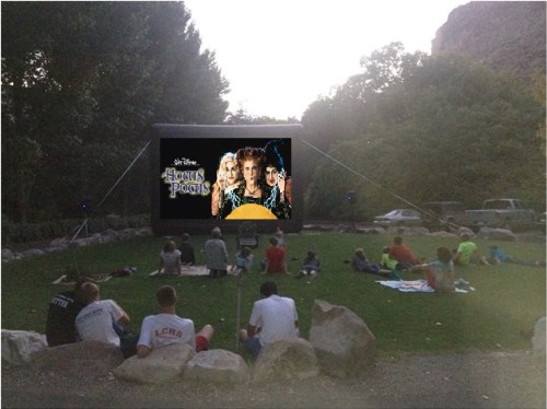 Outdoor movie screening of "Hocus Pocus" with a crowd sitting on the grass, surrounded by trees and rocks.