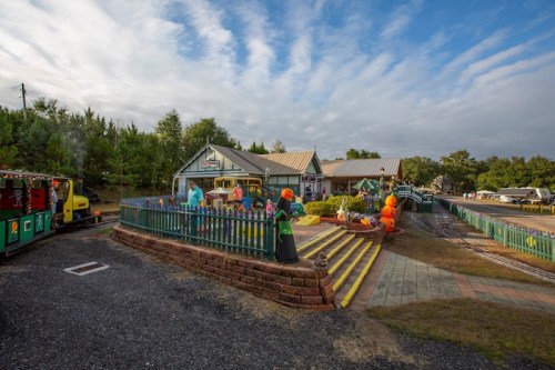 A colorful outdoor scene featuring a shop with a train, surrounded by greenery and playful decorations.