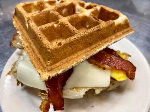 A waffle sandwich filled with bacon, cheese, and an egg, served on a white plate.