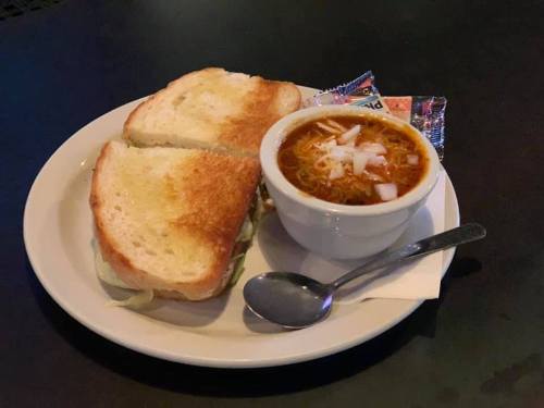 A plate with a toasted sandwich and a bowl of soup, accompanied by a spoon and condiment packets.