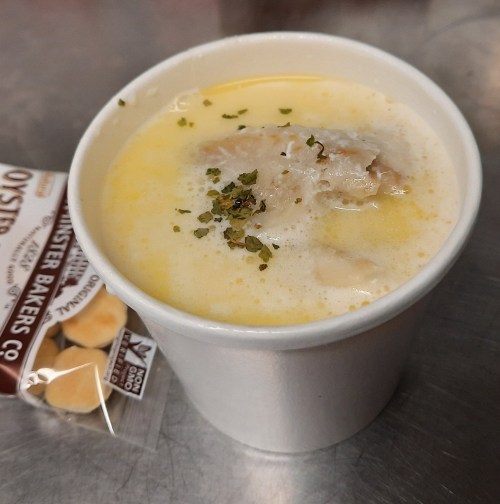 A cup of creamy soup topped with herbs, alongside a small packet of oyster crackers.