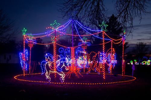 A carousel made of colorful lights, surrounded by trees, glowing against a twilight sky.