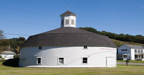 A round, white building with a cupola, set against a clear blue sky and green hills in the background.