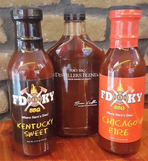 Three bottles of BBQ sauce: Kentucky Sweet, Chicago Fire, and Distillers Blend, displayed against a stone background.