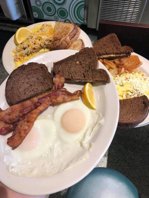 A plate with two fried eggs, bacon, and toast, alongside another plate with scrambled eggs, toast, and hash browns.