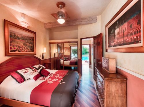 Cozy bedroom with a double bed, wooden furniture, and artwork, leading to a view of a pool outside.