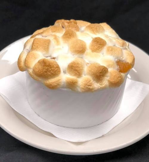 A baked dessert with a golden, toasted marshmallow topping in a white ramekin on a plate.