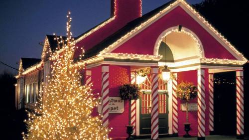 A brightly lit pink building decorated for Christmas, with candy cane accents and a glowing tree in front.