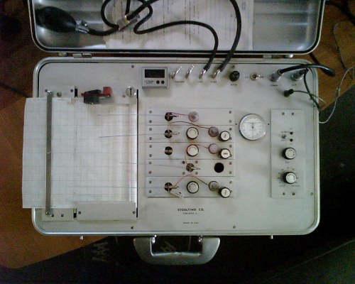 A vintage medical device in a metal case with dials, gauges, and a graph paper for recording data.
