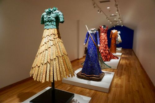A gallery displaying unique, artistic dresses on mannequins, featuring vibrant colors and intricate designs.