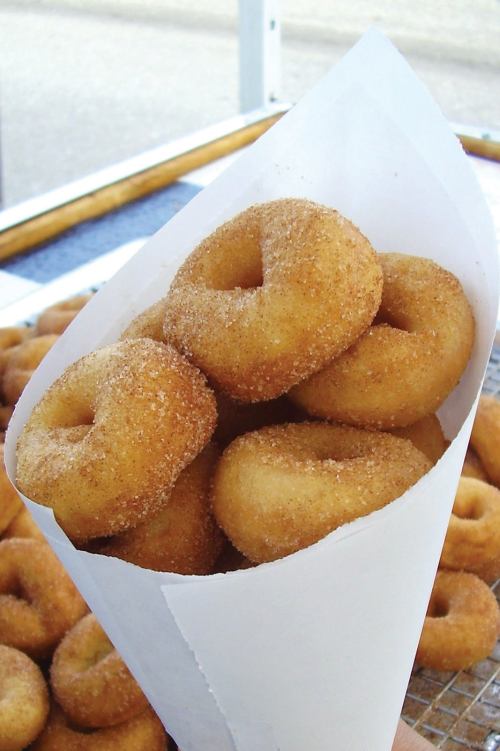A paper cone filled with freshly made, sugar-coated donuts.