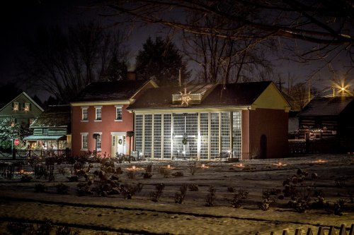 A beautifully lit brick house at night, surrounded by snow and decorated with festive lights and a large star.