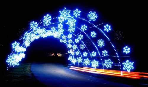 A glowing arch of blue and white snowflake lights over a dark road, creating a festive winter atmosphere.